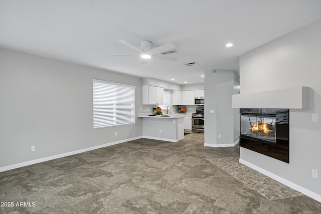 unfurnished living room with a multi sided fireplace, visible vents, baseboards, and ceiling fan