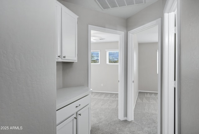 corridor featuring visible vents, light colored carpet, and baseboards