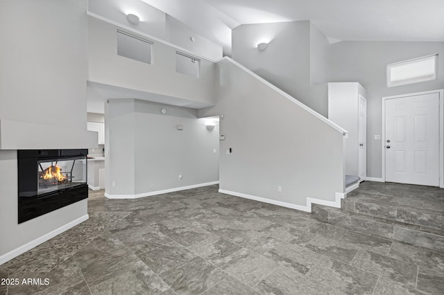 unfurnished living room featuring stairway, baseboards, and high vaulted ceiling