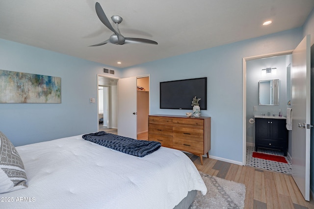 bedroom with connected bathroom, wood finished floors, a ceiling fan, visible vents, and a walk in closet