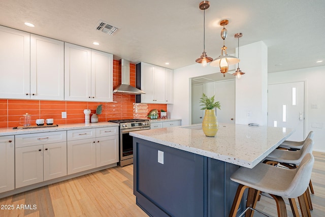 kitchen featuring visible vents, light wood-style floors, a kitchen island, stainless steel gas range, and wall chimney range hood