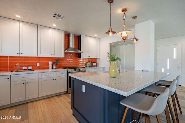 kitchen featuring gas range, wall chimney exhaust hood, light wood-style flooring, a center island, and backsplash