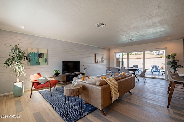 living room with visible vents, brick wall, wood finished floors, a textured ceiling, and recessed lighting