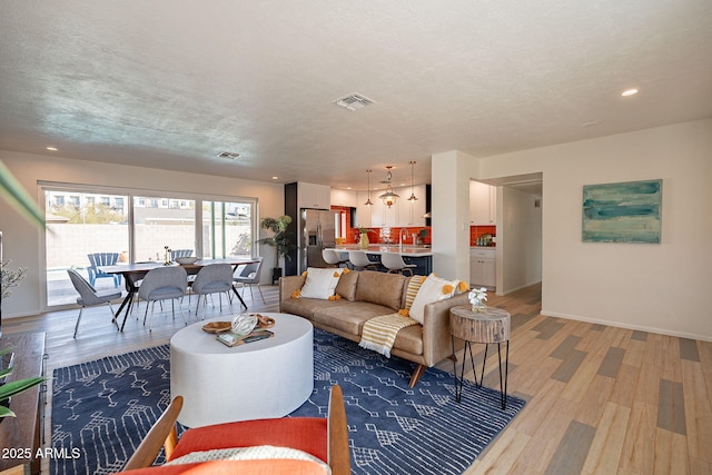 living area with a textured ceiling, recessed lighting, visible vents, baseboards, and light wood finished floors