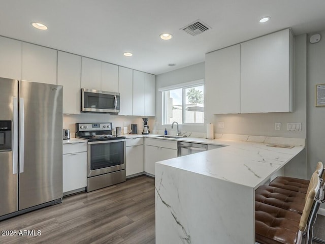 kitchen featuring stainless steel appliances, a peninsula, white cabinets, dark wood-style floors, and recessed lighting