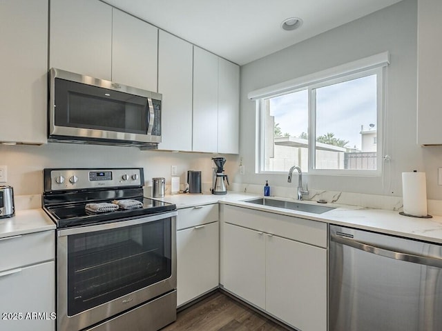 kitchen featuring stainless steel appliances, a sink, dark wood-type flooring, and white cabinetry