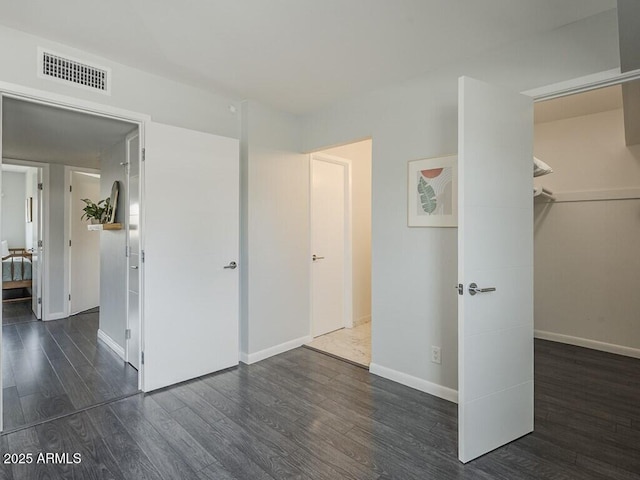 unfurnished bedroom with wood finished floors, baseboards, a walk in closet, and a closet