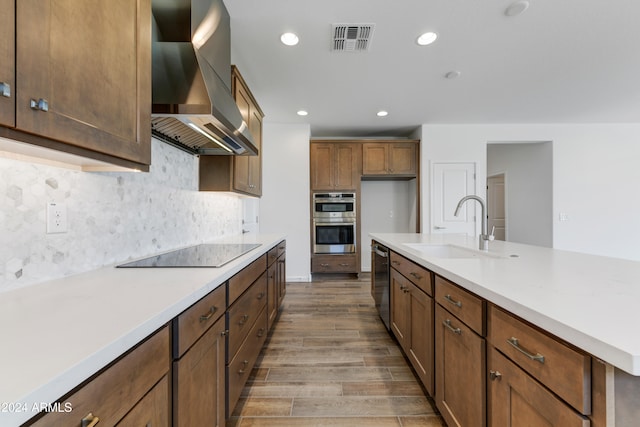 kitchen featuring sink, tasteful backsplash, wall chimney exhaust hood, hardwood / wood-style flooring, and stainless steel appliances