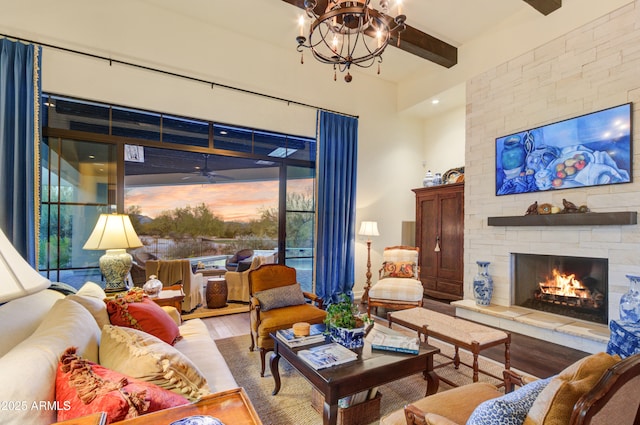 living room with light wood-type flooring, an inviting chandelier, a stone fireplace, and beamed ceiling