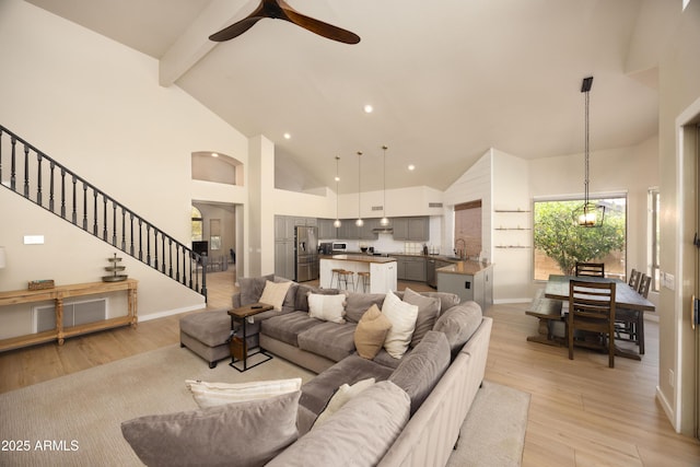 living room featuring beamed ceiling, a ceiling fan, high vaulted ceiling, and stairs