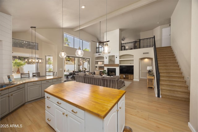 kitchen with butcher block countertops, light wood-style floors, a center island, and high vaulted ceiling