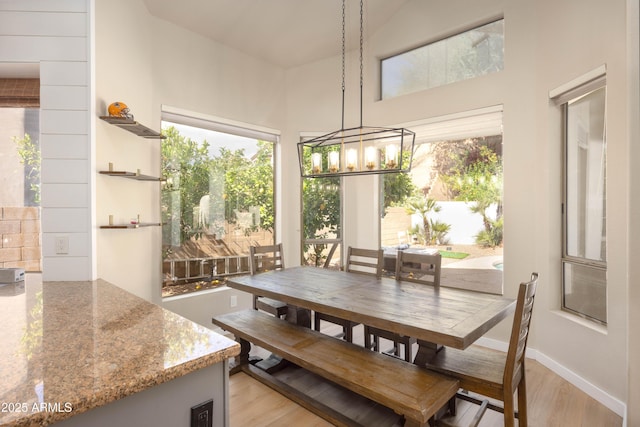 dining room with baseboards, a high ceiling, an inviting chandelier, and light wood-style floors