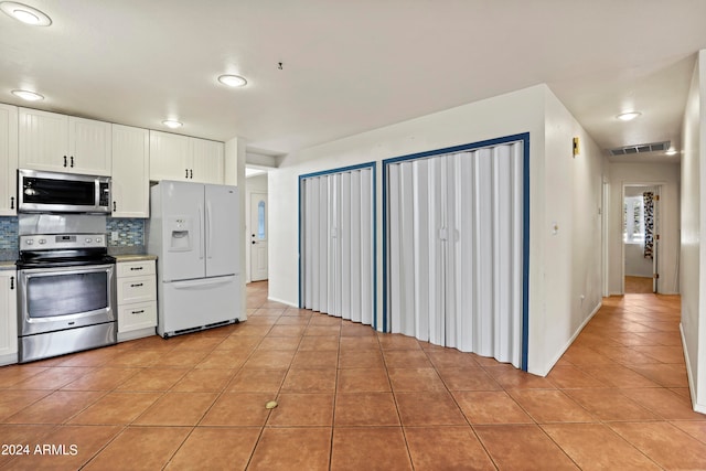 kitchen with appliances with stainless steel finishes, decorative backsplash, light tile patterned floors, and white cabinets