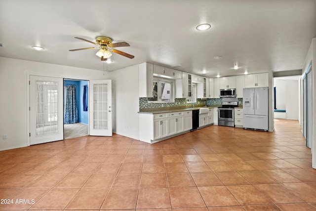 kitchen with ceiling fan, stainless steel appliances, white cabinets, light tile patterned flooring, and backsplash