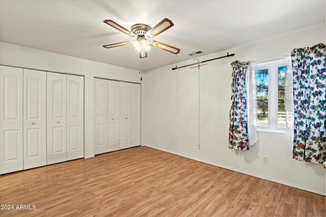 unfurnished bedroom with ceiling fan, multiple closets, and light wood-type flooring