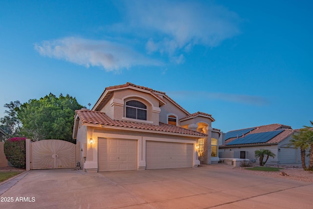 mediterranean / spanish house featuring driveway, stucco siding, a gate, and a tiled roof