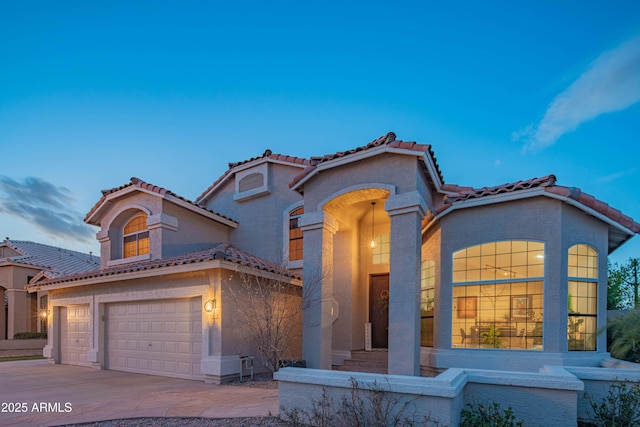 mediterranean / spanish-style home with a garage, driveway, a tile roof, and stucco siding