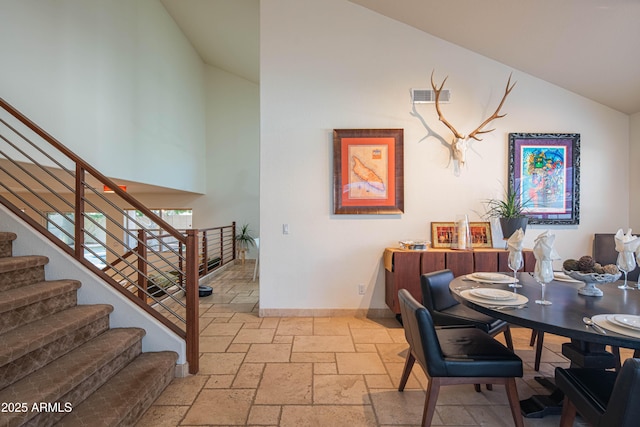 dining space with stone tile floors, visible vents, stairway, high vaulted ceiling, and baseboards