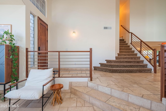 foyer entrance featuring stairway, visible vents, a towering ceiling, and stone tile floors