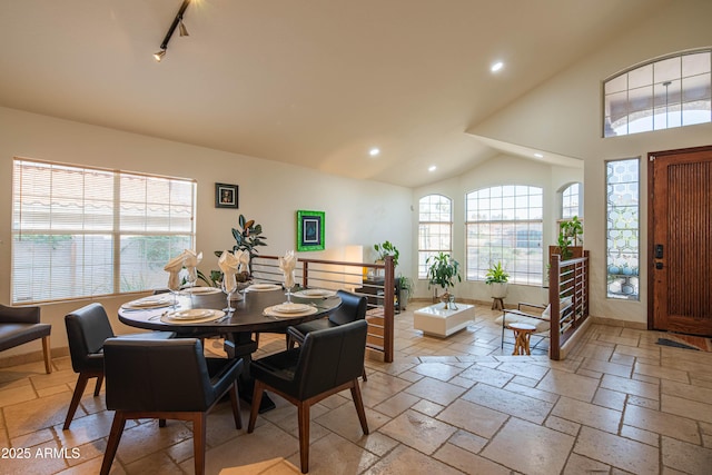 dining room with baseboards, rail lighting, vaulted ceiling, stone tile flooring, and recessed lighting