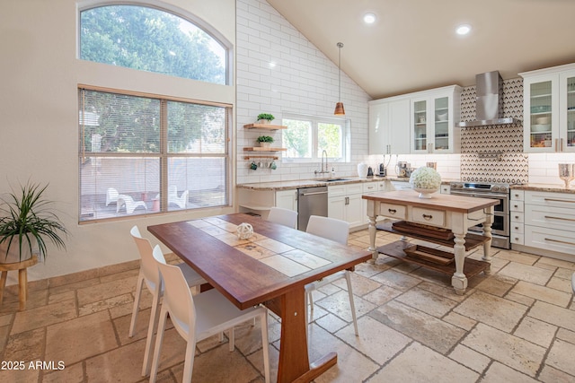 kitchen featuring stainless steel appliances, stone tile flooring, decorative backsplash, and wall chimney exhaust hood