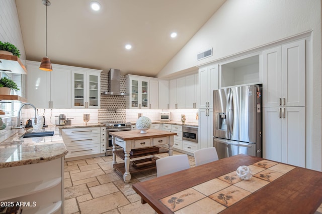 kitchen featuring stone tile floors, stainless steel appliances, visible vents, a sink, and wall chimney range hood