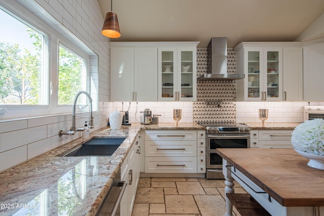 kitchen with stone tile floors, a sink, butcher block countertops, double oven range, and wall chimney exhaust hood