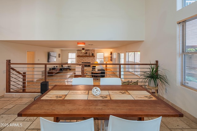 dining room with a large fireplace, stone tile floors, a towering ceiling, and a healthy amount of sunlight