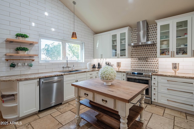 kitchen with stone tile floors, butcher block countertops, wall chimney range hood, appliances with stainless steel finishes, and open shelves