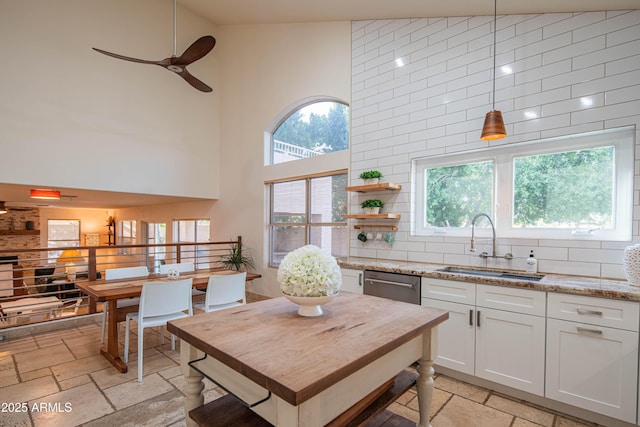 kitchen with stone tile flooring, backsplash, a sink, ceiling fan, and dishwasher