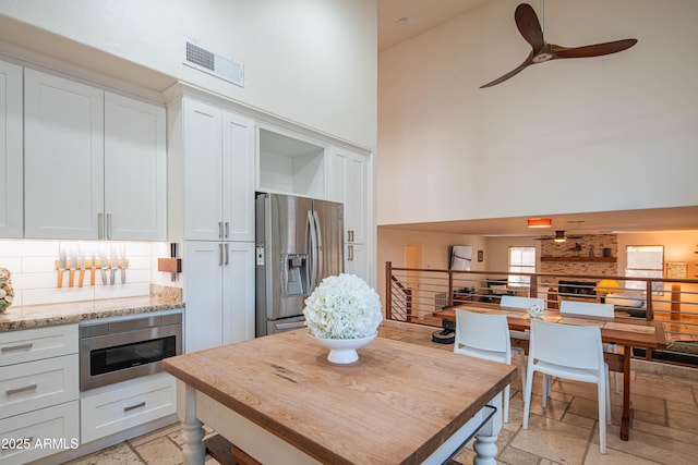 kitchen with appliances with stainless steel finishes, a high ceiling, visible vents, and stone tile floors