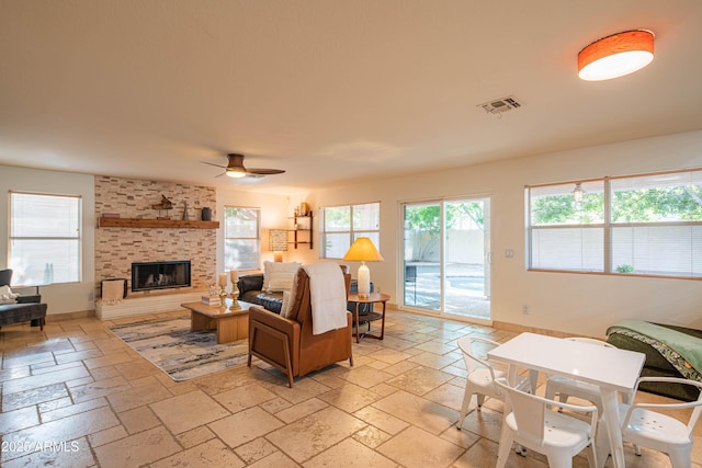 living room with visible vents, a wealth of natural light, a brick fireplace, and stone tile flooring