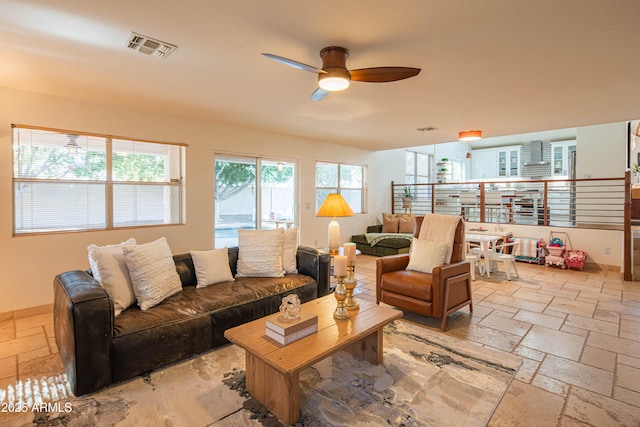 living room featuring a ceiling fan, stone tile flooring, visible vents, and baseboards