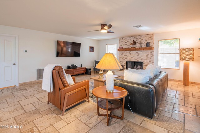 living room with a ceiling fan, a fireplace, visible vents, and stone tile floors