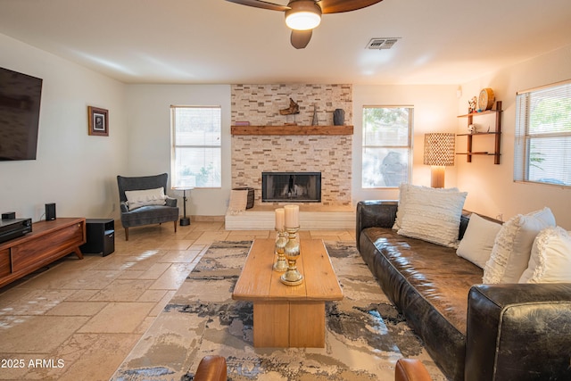 living area featuring a ceiling fan, baseboards, visible vents, a brick fireplace, and stone tile flooring