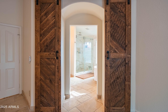 hallway featuring baseboards, stone tile floors, and a barn door