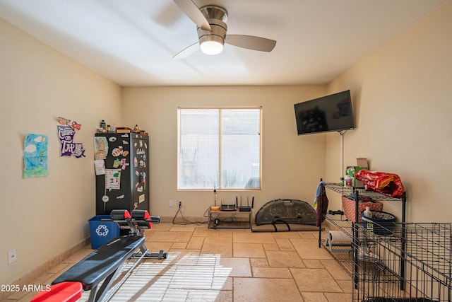 workout area with baseboards, stone tile flooring, and a ceiling fan