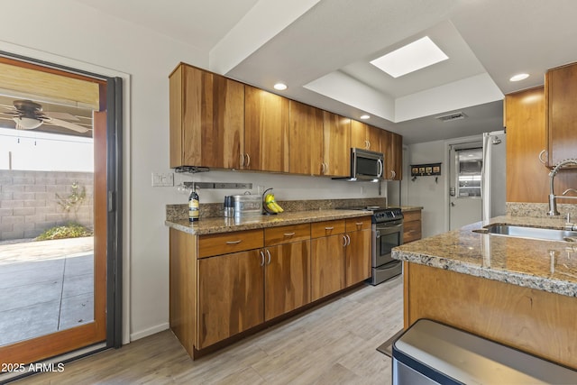 kitchen featuring light stone counters, visible vents, appliances with stainless steel finishes, brown cabinetry, and a sink