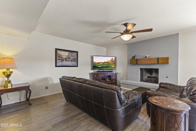 living area with a fireplace with raised hearth, a ceiling fan, vaulted ceiling, wood finished floors, and baseboards