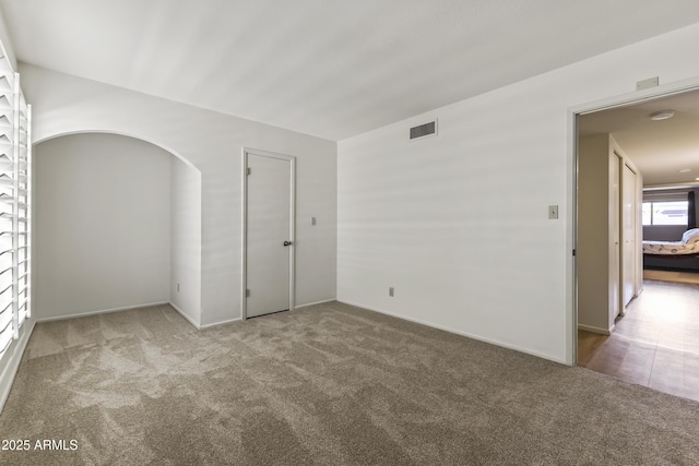 carpeted empty room featuring arched walkways and visible vents