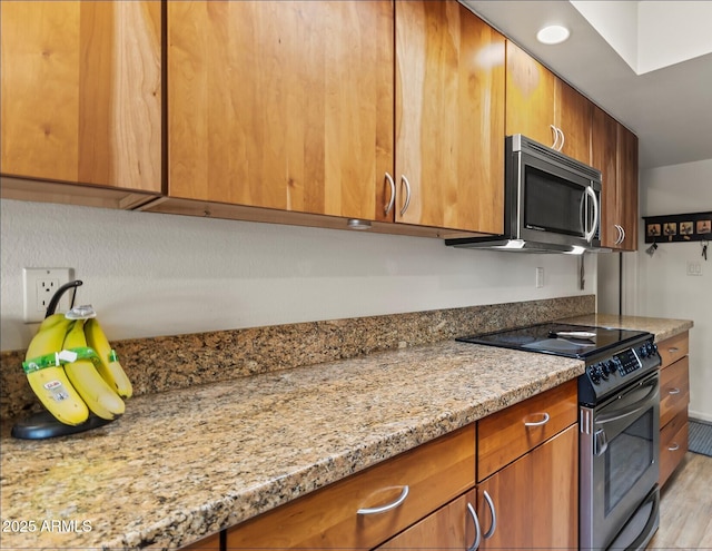 kitchen with brown cabinetry, electric stove, stainless steel microwave, and light stone countertops