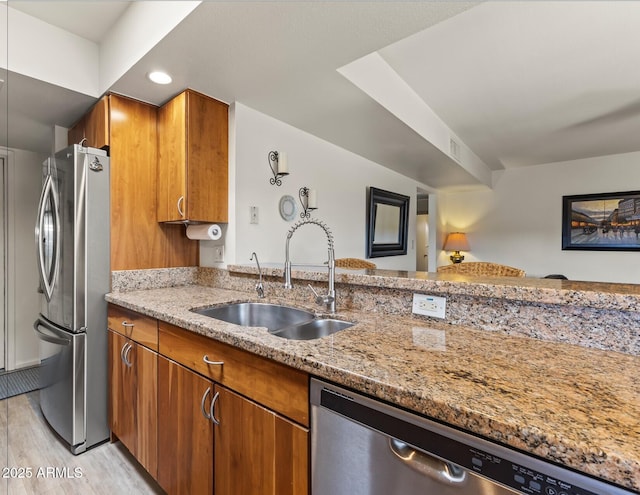 kitchen featuring brown cabinets, light stone countertops, stainless steel appliances, light wood-type flooring, and a sink