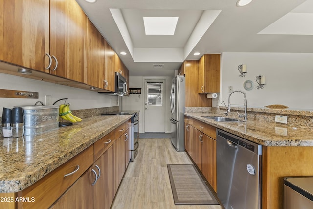 kitchen featuring appliances with stainless steel finishes, a tray ceiling, brown cabinetry, and a sink