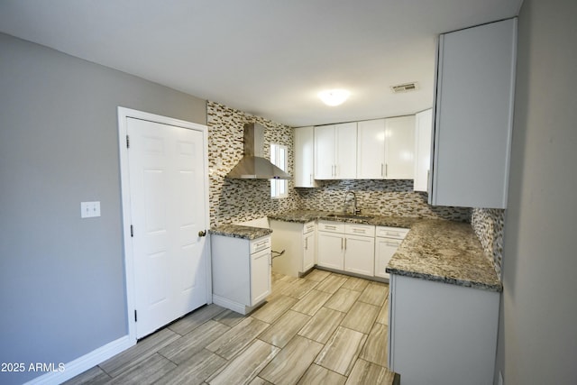 kitchen featuring white cabinets, backsplash, sink, and wall chimney exhaust hood