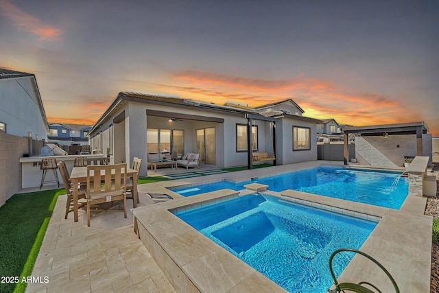 back of property at dusk featuring a patio, a pool with connected hot tub, area for grilling, an outdoor hangout area, and a fenced backyard