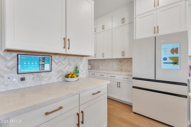 kitchen with light wood-style floors, tasteful backsplash, white cabinetry, and freestanding refrigerator