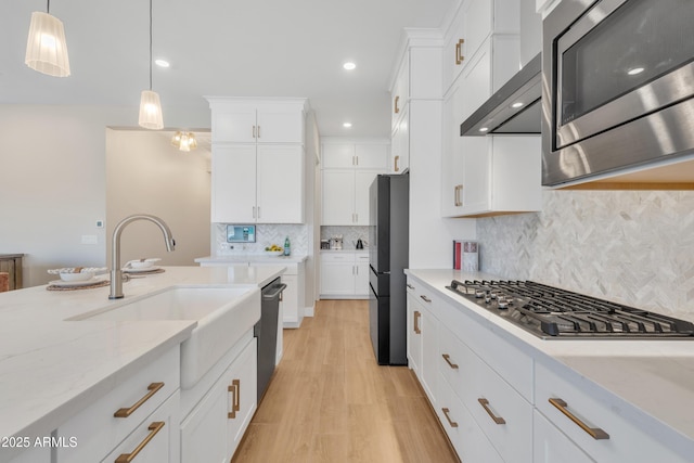 kitchen featuring appliances with stainless steel finishes, light stone countertops, white cabinetry, pendant lighting, and a sink