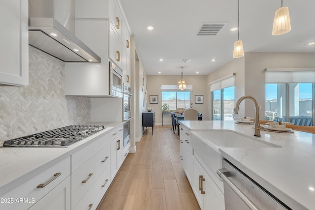 kitchen with visible vents, white cabinets, appliances with stainless steel finishes, light stone countertops, and wall chimney exhaust hood