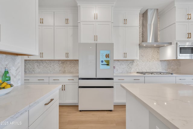 kitchen featuring stainless steel appliances, decorative backsplash, white cabinets, light wood-type flooring, and wall chimney exhaust hood