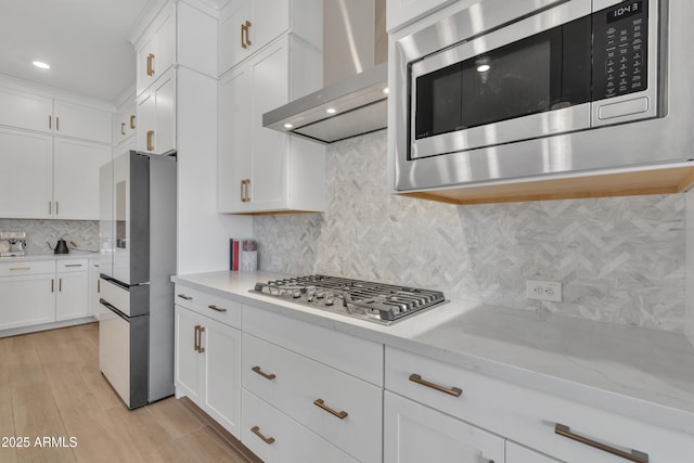 kitchen with light wood finished floors, light stone countertops, stainless steel appliances, wall chimney range hood, and white cabinetry